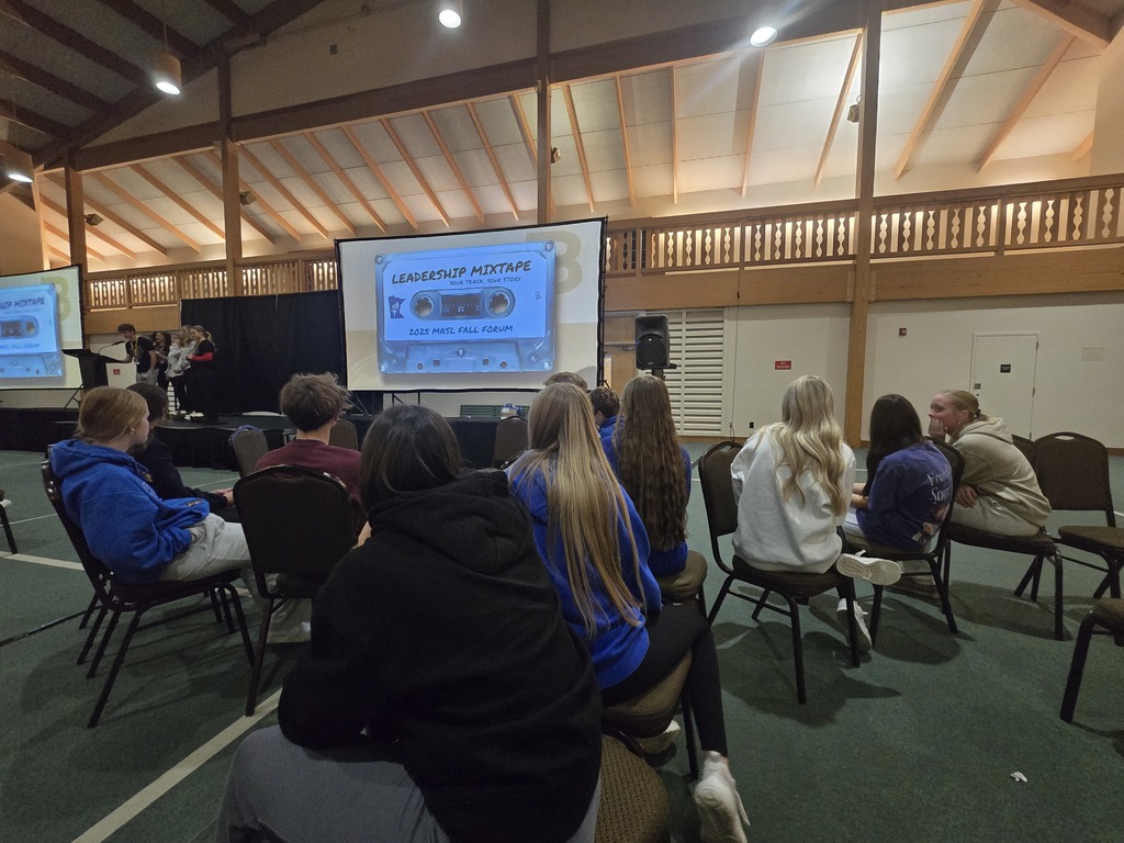 students in a circle watching a presentation on the screen.