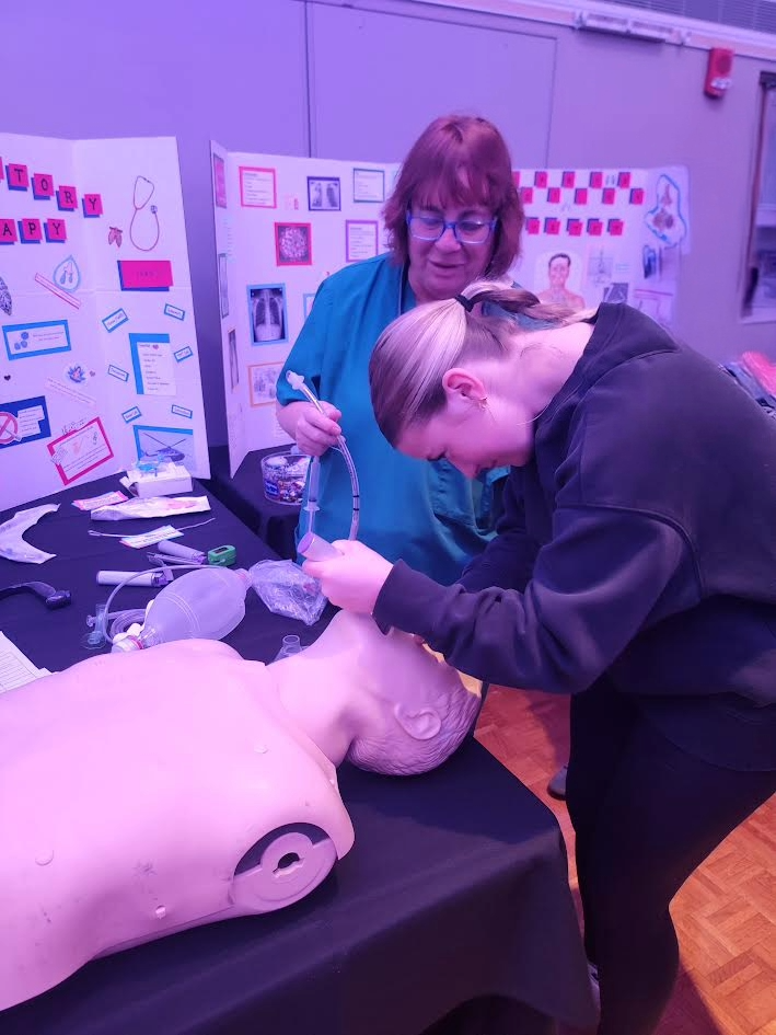 students and a nurse looking into a practice medical doll's mouth.