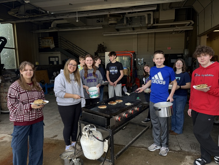 students frying pancakes on a griddle smiling at camera 