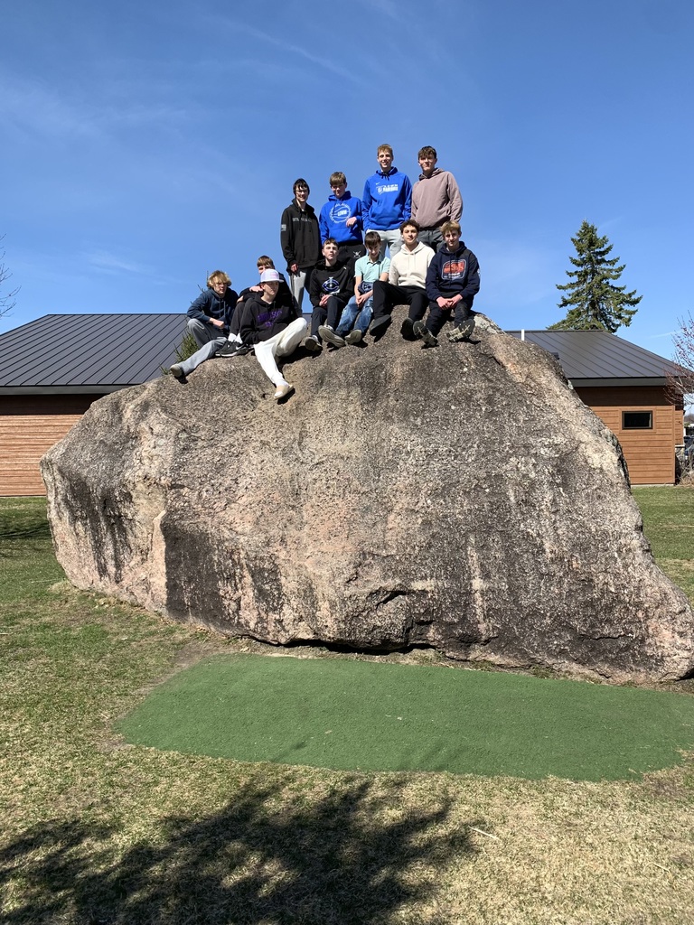 Students sitting on a big rock outside of the hormel nature center. 