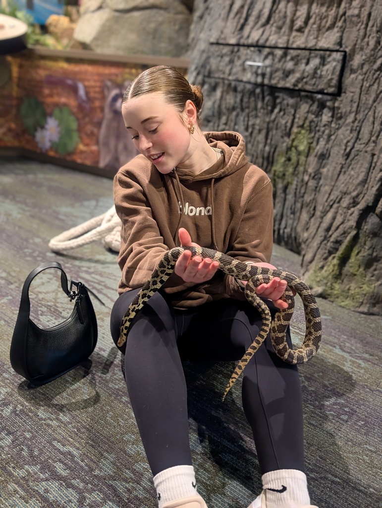Students sitting on the floor holding a snake. 