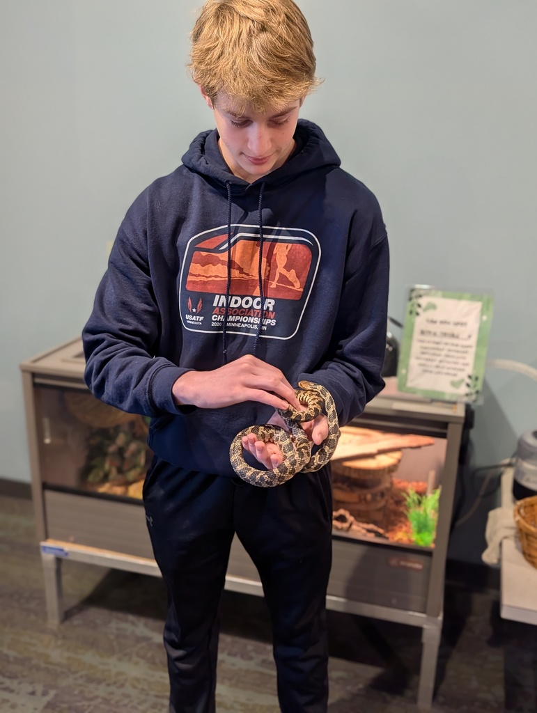 Student holding a snake while standing in front of an aquarium at the Hormel Nature Center. 