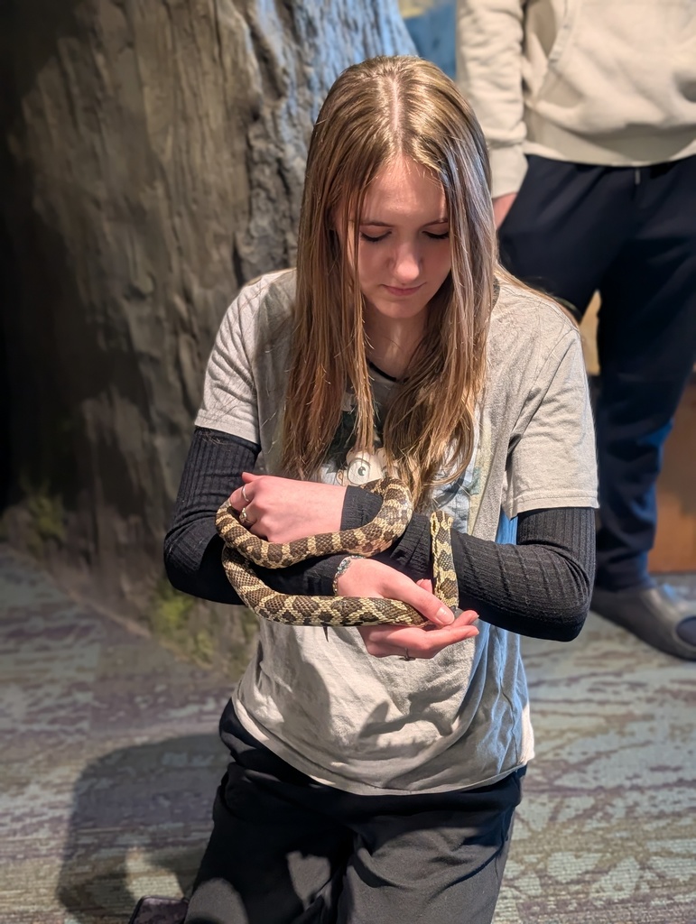 Students sitting on the floor holding a snake. 