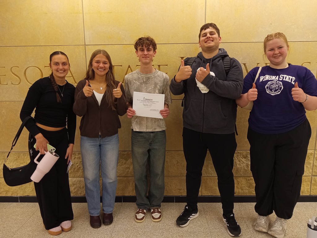 Students lined up against the wall holding thumbs up after the math competition. 