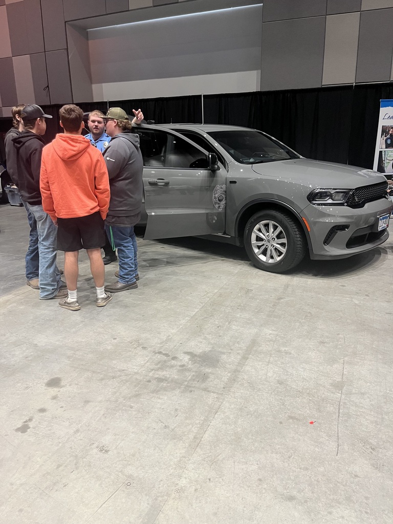 four boys standing and talking to a man in front of a gray mini van with the door propped open with damage near the hinge.  