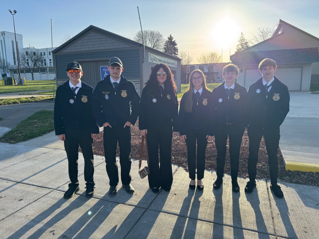 Six students standing on a concrete pad with the sun shining behind them in their official FFA dress. 