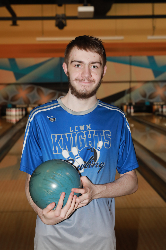 Phynix holding a bowling ball smiling in front of the lanes.