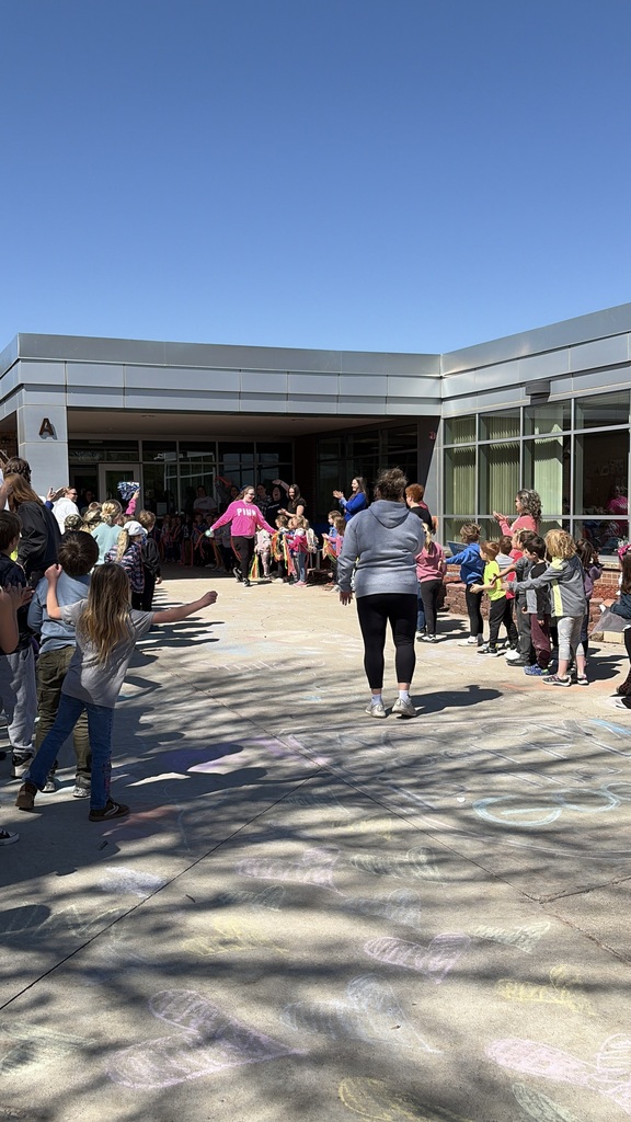Carynn is walking out of the building high fiving a bunch of students standing outside of the school.  