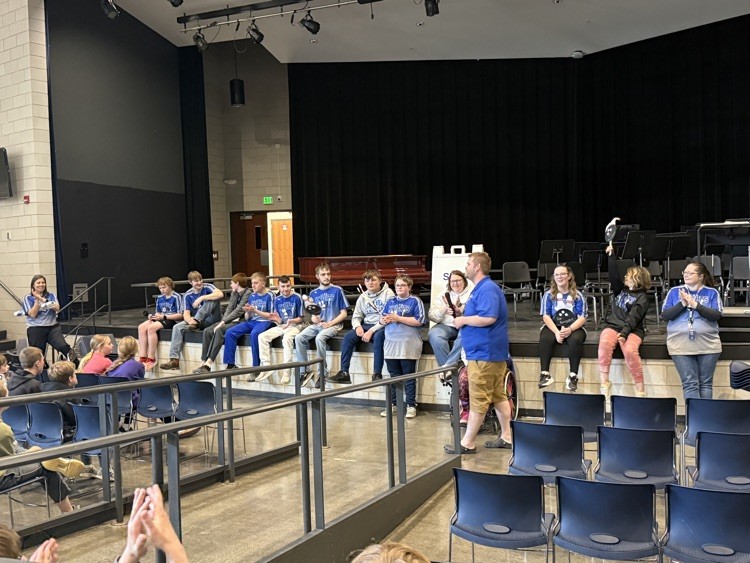 students lined up on the front of an auditorium stage while one person is holding the mic, talking about the bowling season  