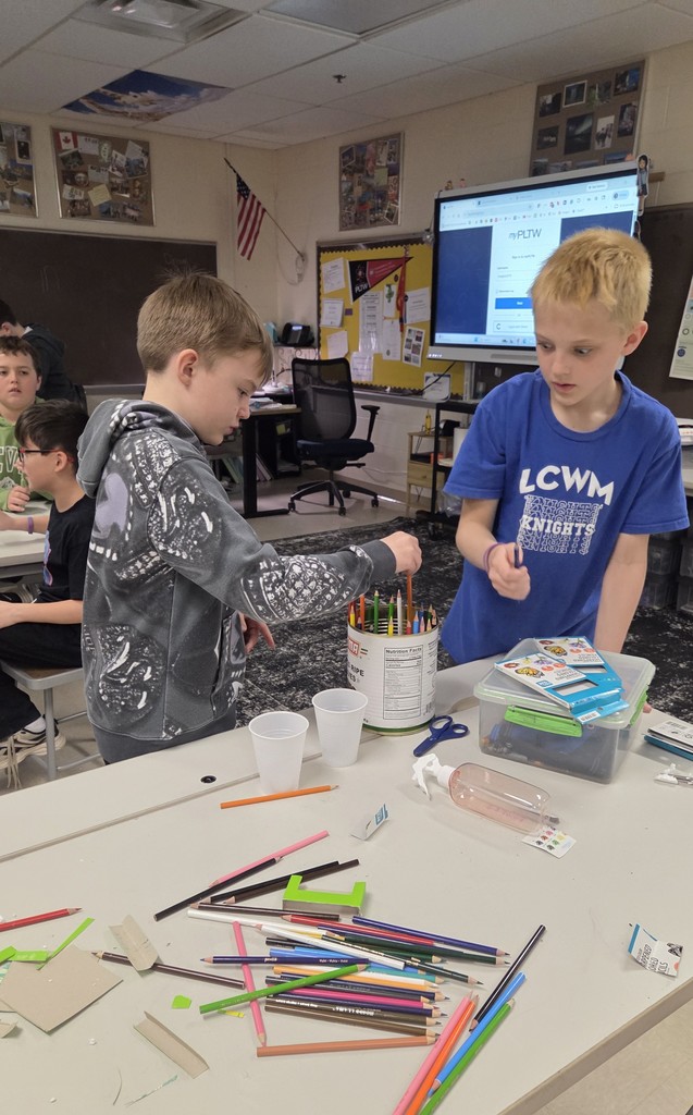 Students working with their hands on a project, stacking pencils into a bucket.