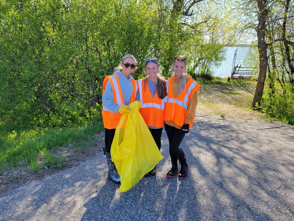 Students holding yellow garbage bags with orange vests on in the ditch picking up garbage.
