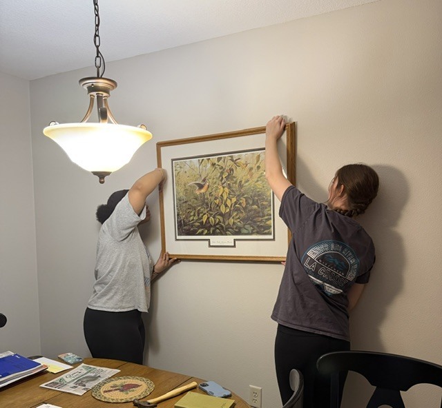 Students hanging up a photo on a blank white wall.