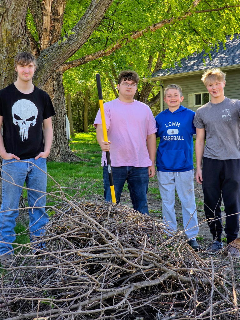 Students behind a stick pile holding a rake. 
