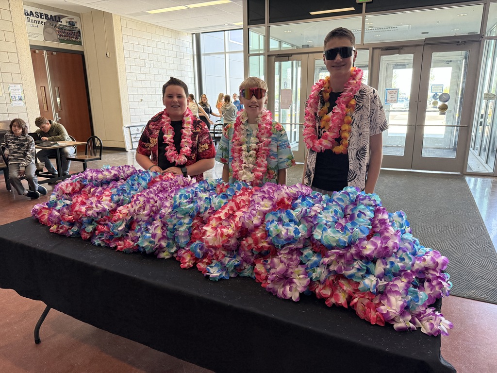 Three students behind a table with a stack of leis on the table. 