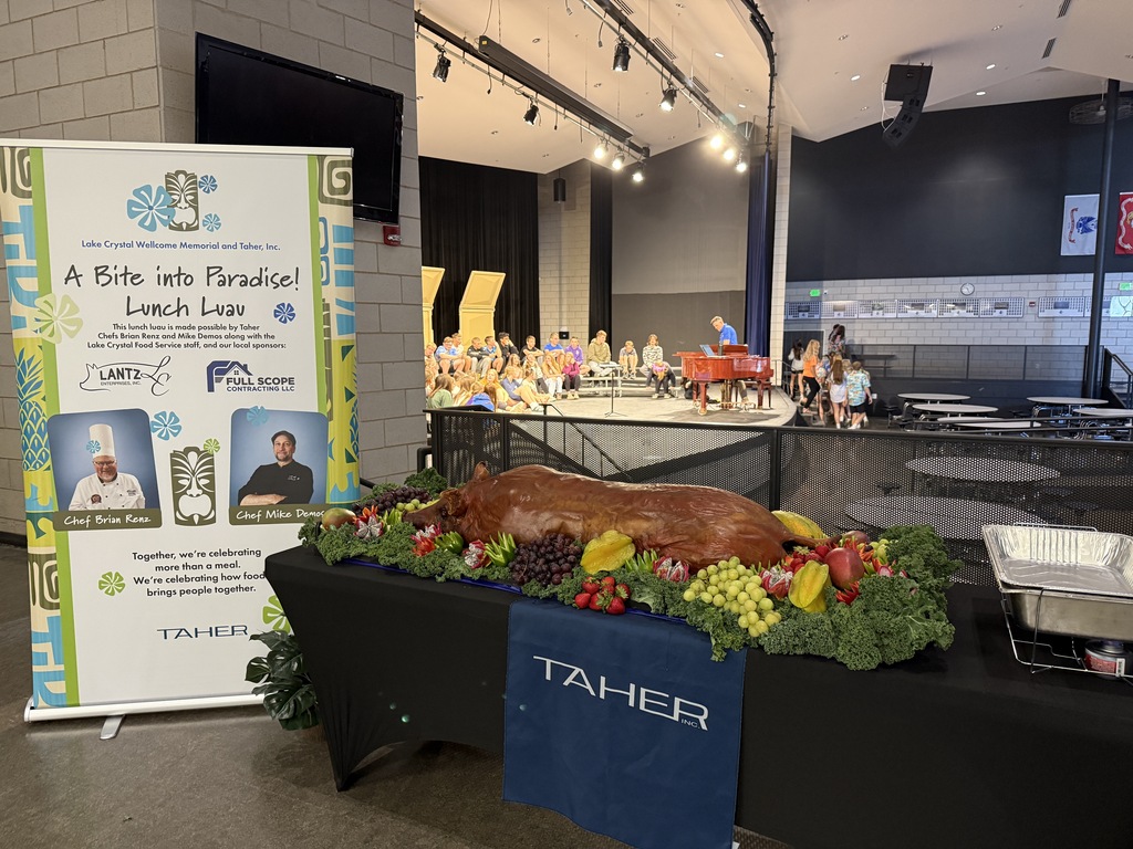 A whole roasted hog on a table with a Taher tablecloth with a banner that says "A Bite into Paradise" with photos of the two chefs.  The hog is garnished with fruit and greens.