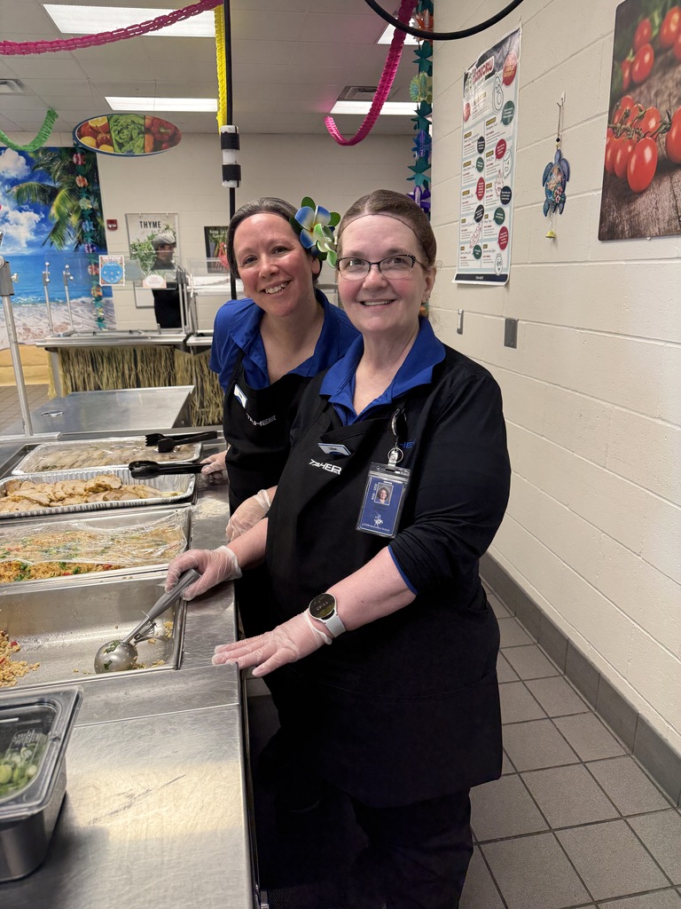 Two lunch ladies serving hawaiian themed food.