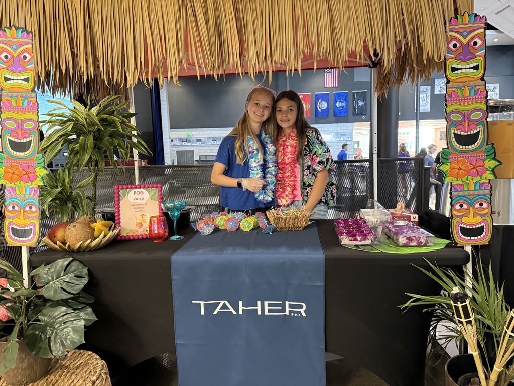 Students standing under a tiki tent preparing to serve the hawaiian drinks to students at lunch time. 