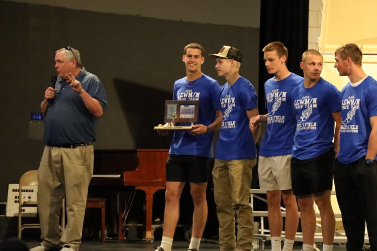 coach burns speaking into a mic while the team stands on the stage behind him  