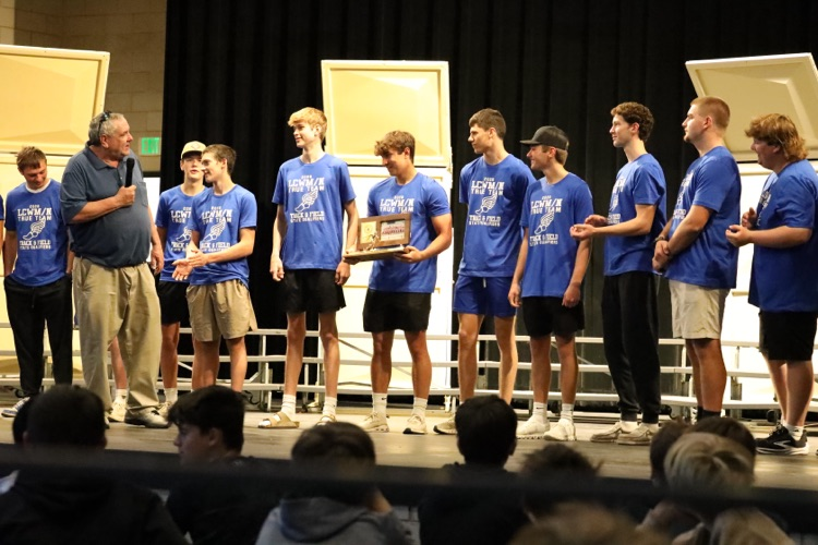 coach burns speaking into a mic while the team stands on the stage behind him. 