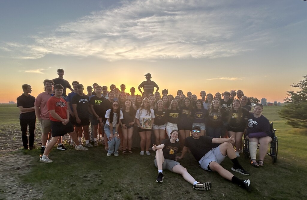 Group of seniors standing in front of the sunset near the football field. 