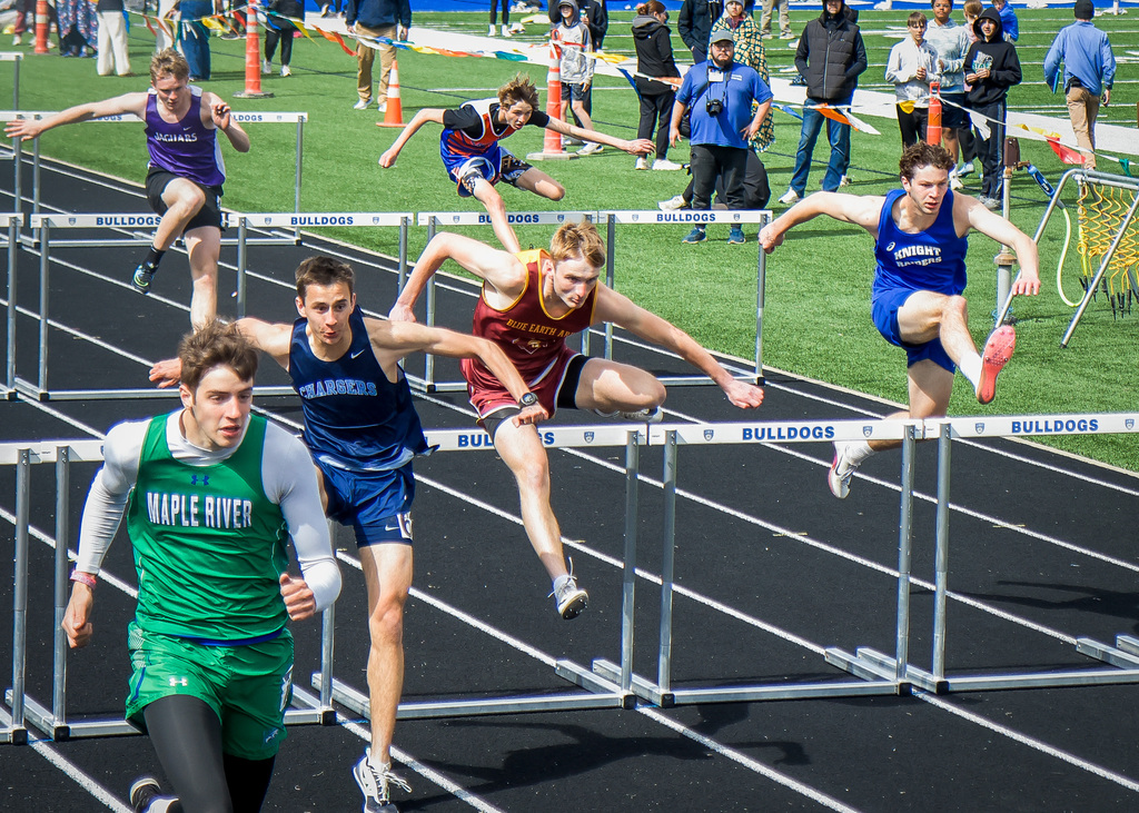 boy running and jumping over hurdles on a track.