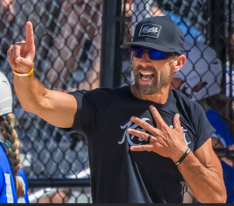 Coach holding up finger signaling "1" with hand on his chest.  Looking towards a batter.  