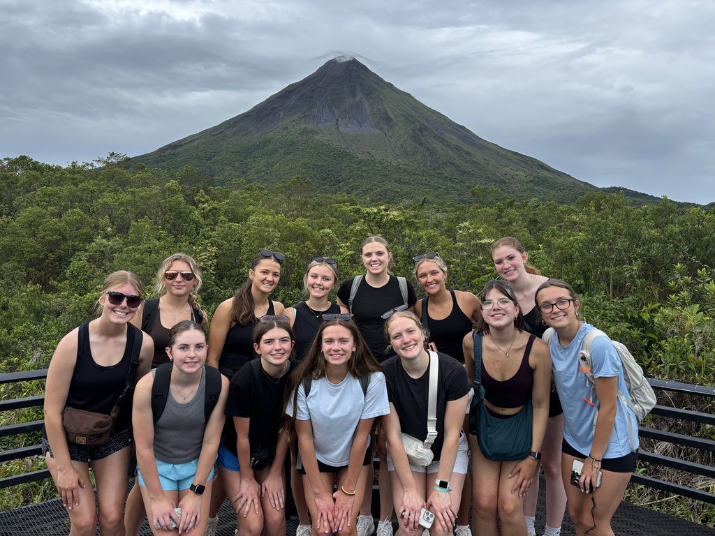 students posing in front of a mountain looking and smiling at camera. 