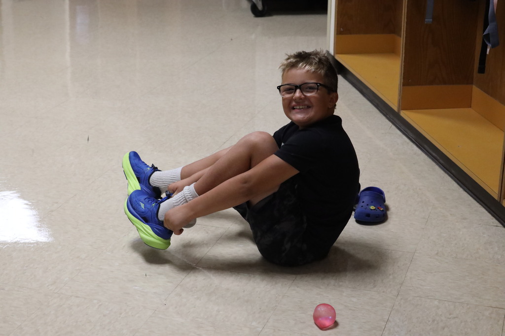 student putting his shoes on in the hall looking at the camera and smiling.