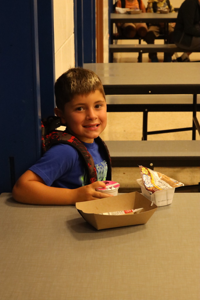 student sitting at the breakfast table with empty containers in front of him, smiling at the camera. 
