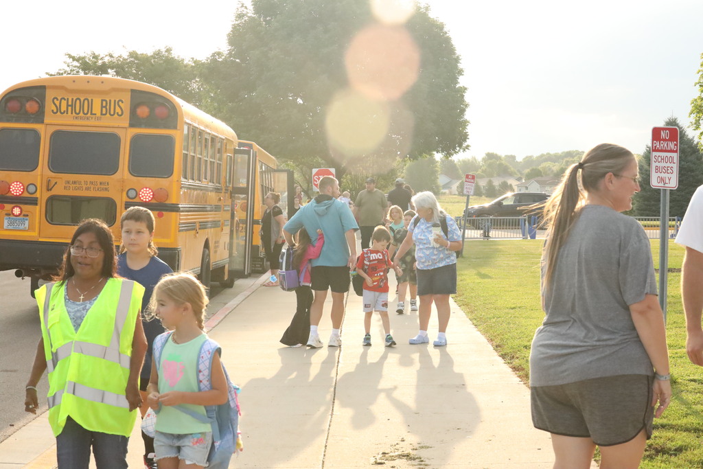Students walking in to school, giving hugs to teachers, and the back of the bus facing the camera.  The photo has the sun shining bright! 