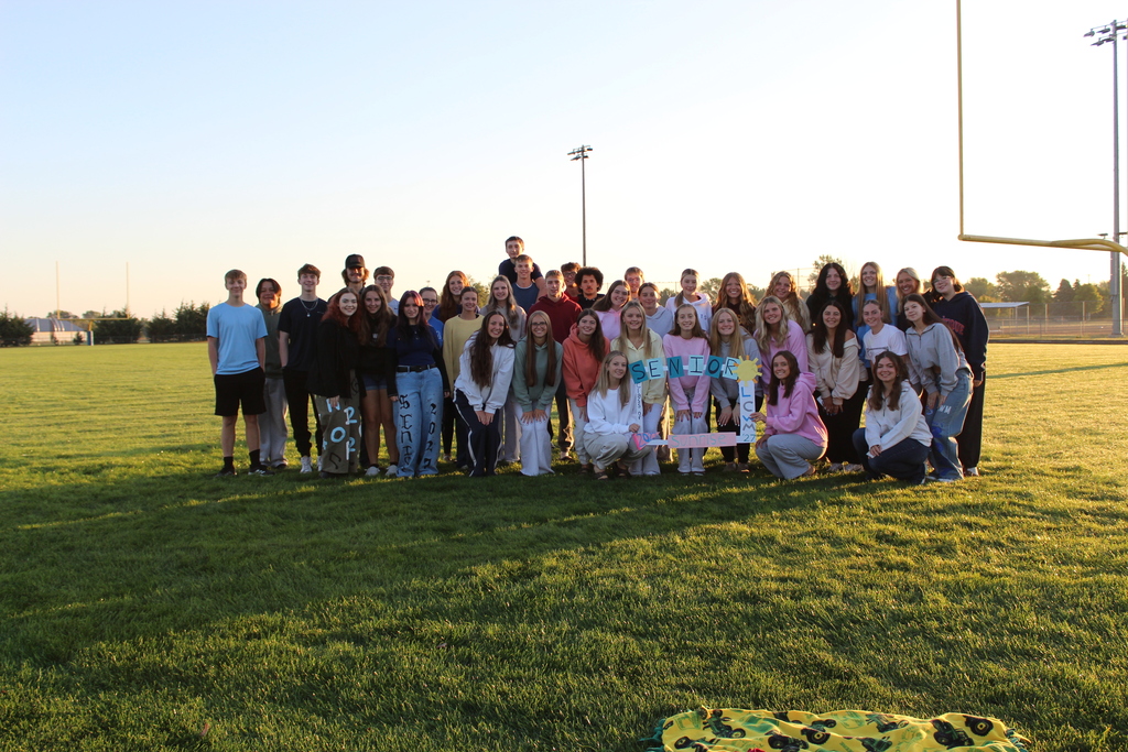 Seniors standing in a group on the football field smiling at the camera holding a sign that said senior sunrise. 