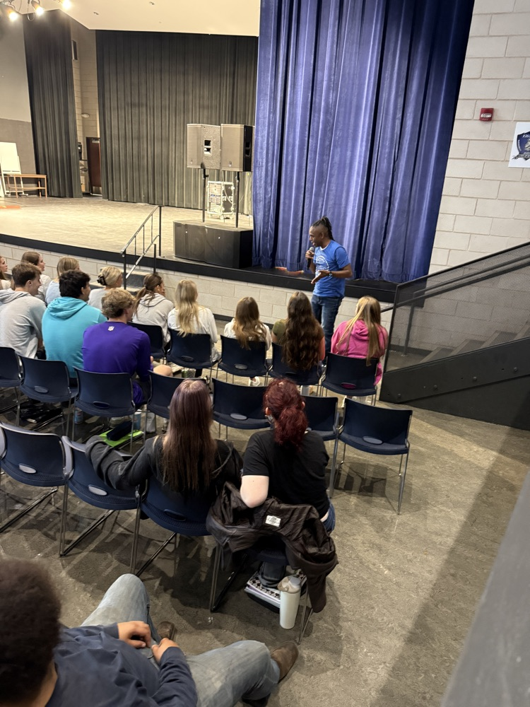 Terrance standing on the ground in front of the stage and in front of the students speaking