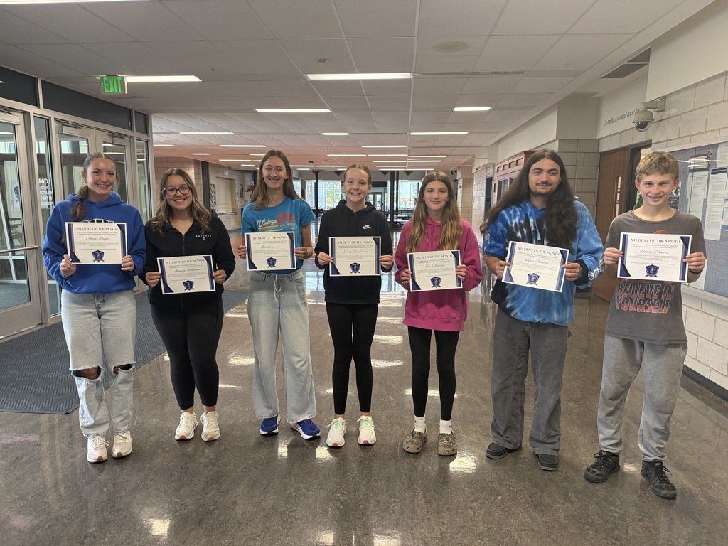 Students standing in a hallway in a line each holding their certificates.