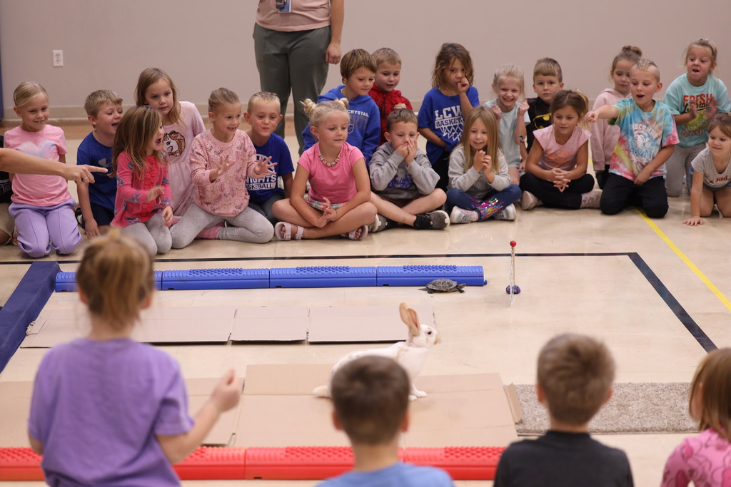 kids sitting around a cardboard race track with a turtle and a rabbit racing eachother.