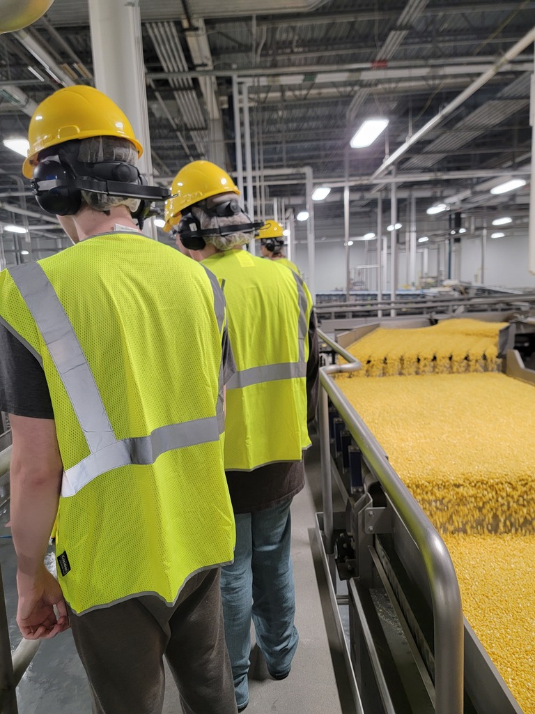Students standing in manufacturing plant listening to speakers