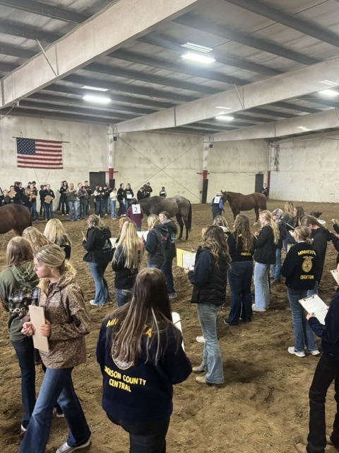 Students in a horse arena watching the judging.