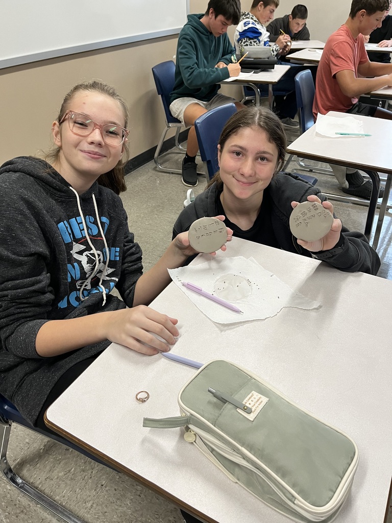 Students, looking and smiling at camera holding clay circle with cuneiform writing on it.
