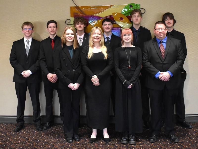 students dressed professionally, standing in a line and smiling at the camera.