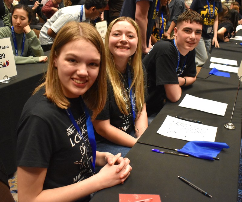 Students at a table taking a quiz. Looking and smiling at camera.