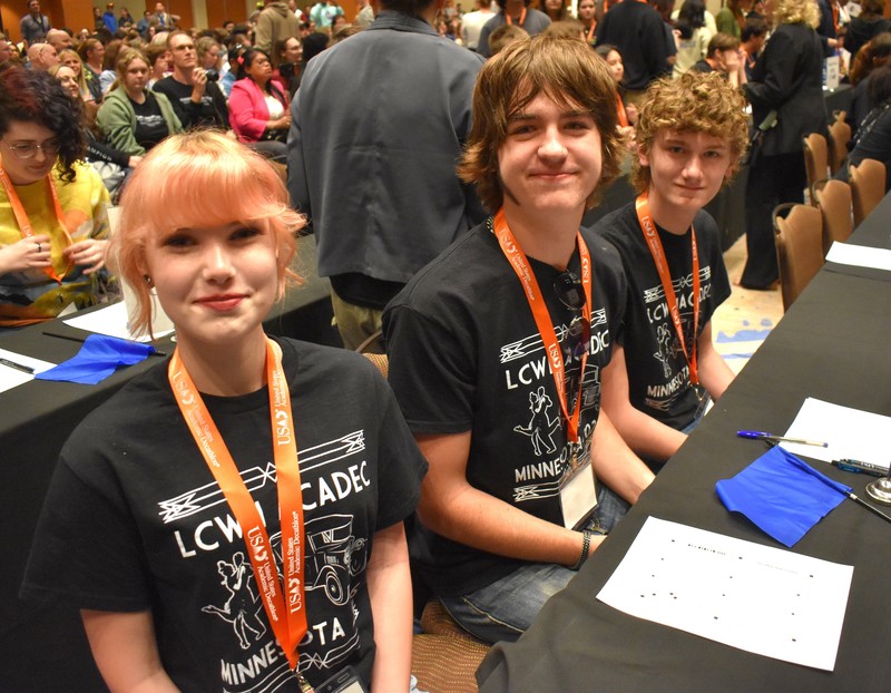 Students at a table taking a quiz. Looking and smiling at camera.