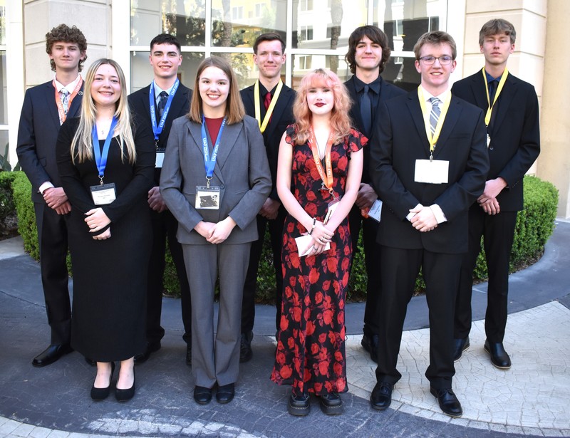 students dressed in formal attire standing, looking at the camera.