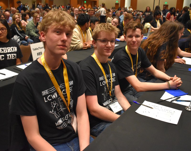 Students at a table taking a quiz. Looking and smiling at camera.