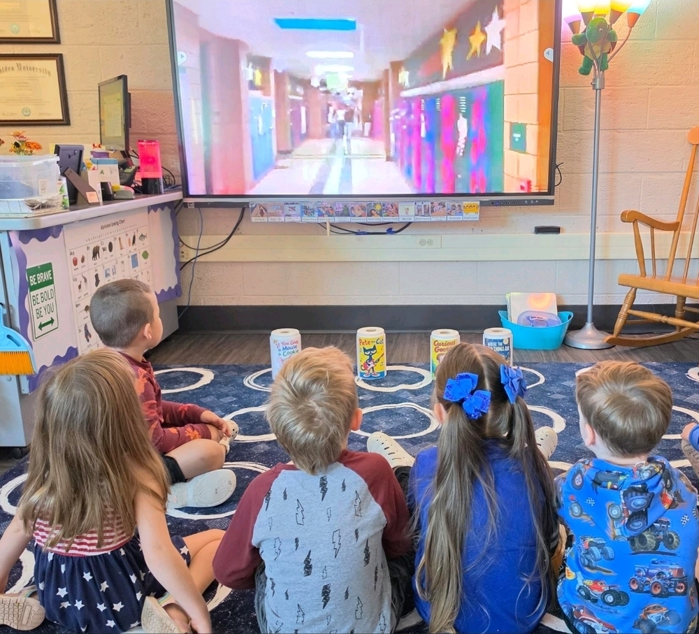 preschool students sitting on a rug watching a video