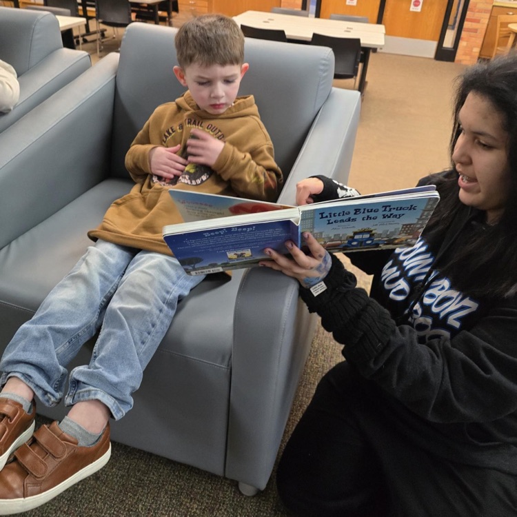 middle school student reading a book to a little boy