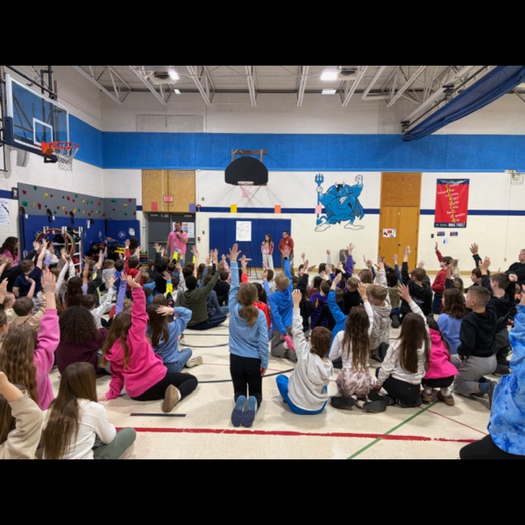 students at an assembly in a gym raising their hands