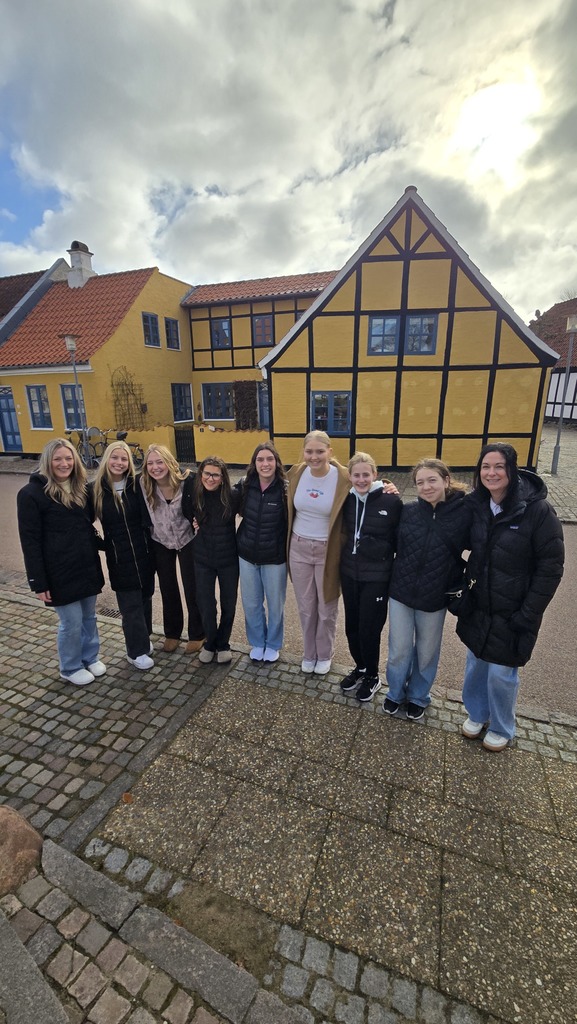group of students posing in front of a yellow house