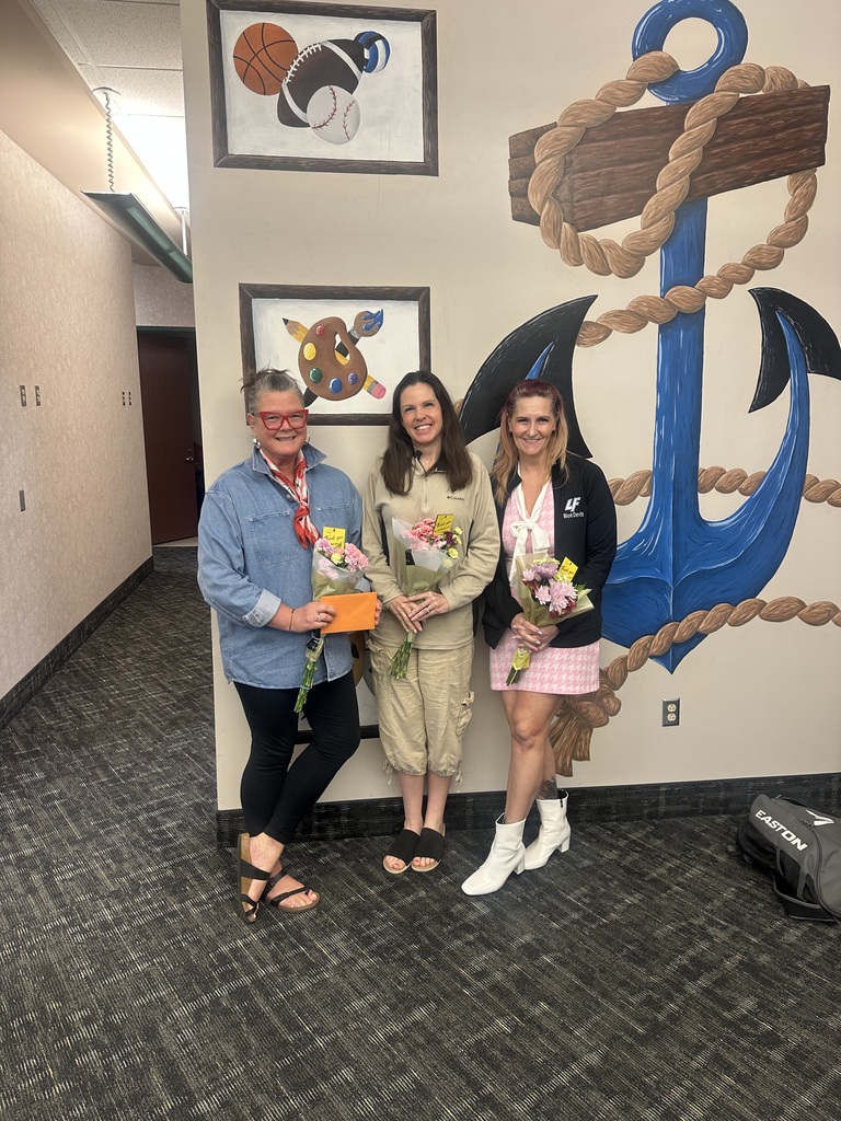 3 women posing with flowers in front of a painting of an anchor
