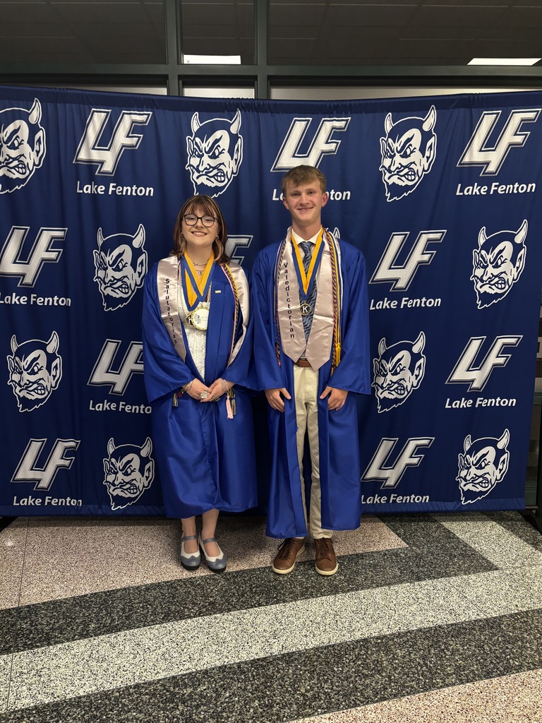 2 high schoolers posing in graduation gown in front of LF backdrop