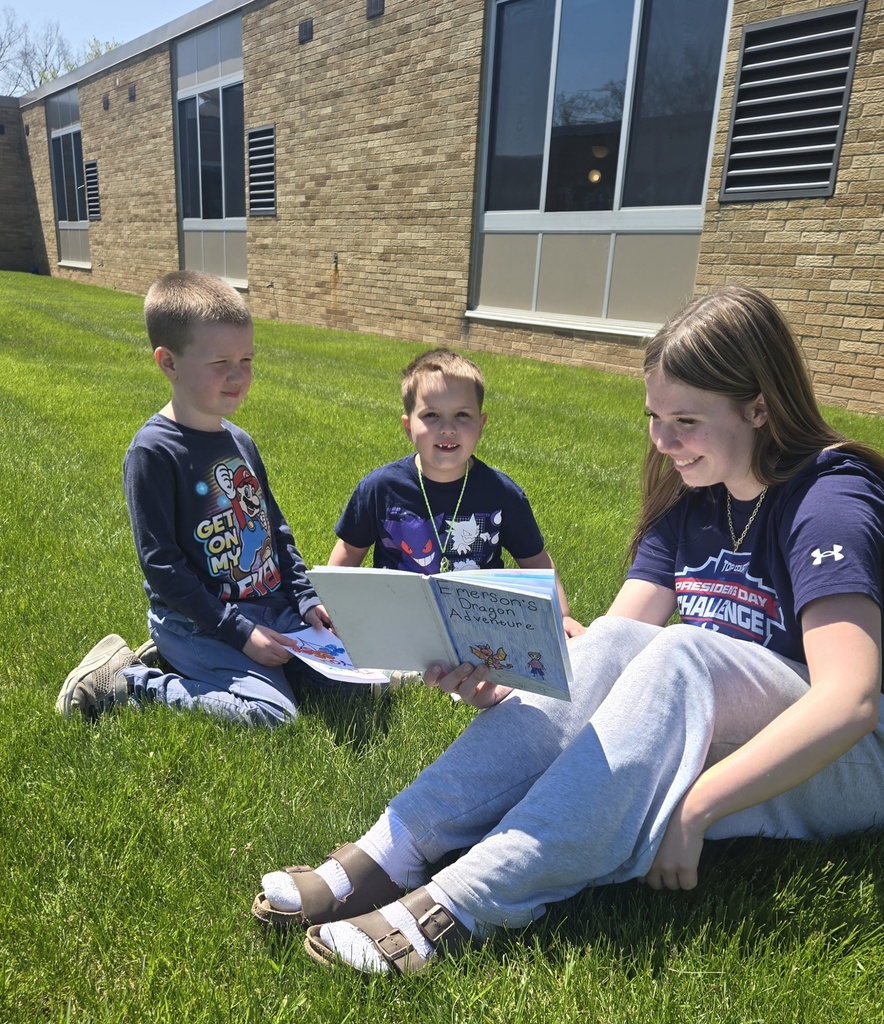 Middle school girl reading in the grass with 2 first grade boys