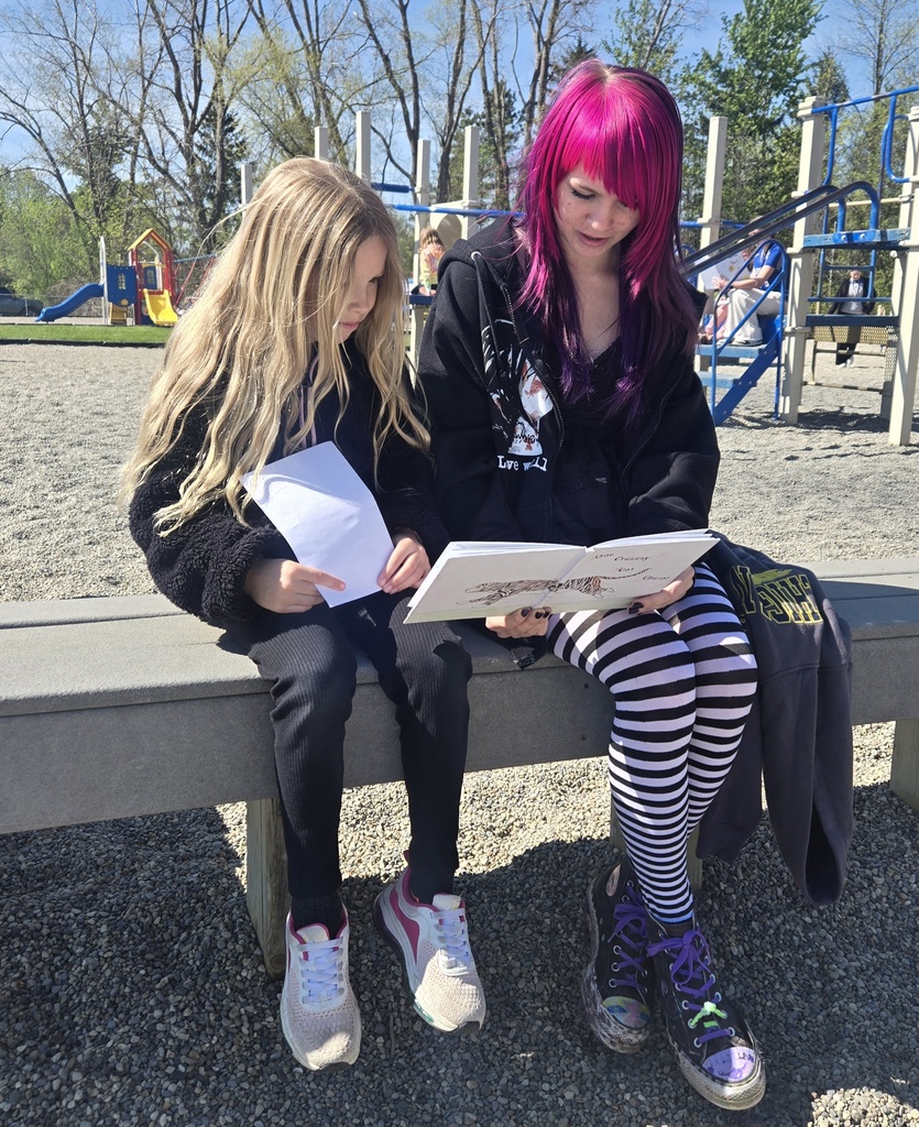 MIddle school girl reading on a playground with a first grade girl